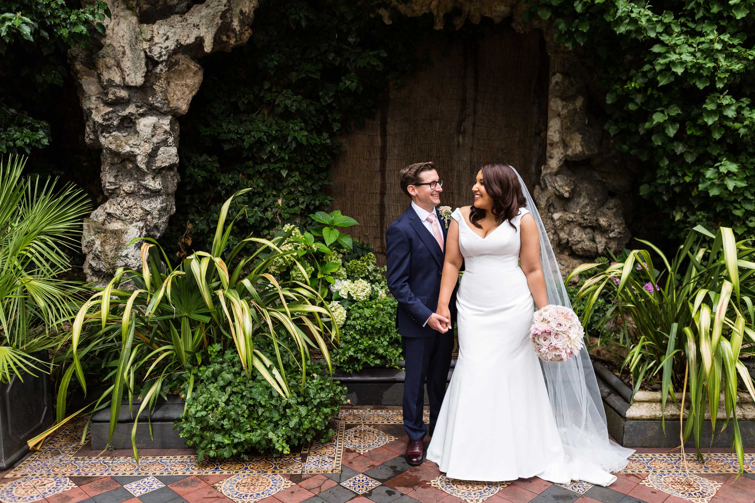 A newlywed couple smile at each other in a garden on their wedding day
